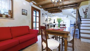 Un accogliente soggiorno con un divano rosso, un tavolo da pranzo in legno e sedie, una cucina sullo sfondo e una scala che conduce a un piano superiore.