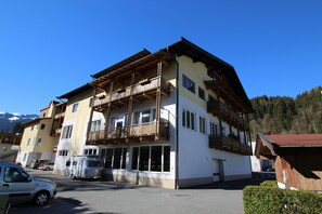Un edificio de varios pisos con balcones, zona de estacionamiento y montañas al fondo.