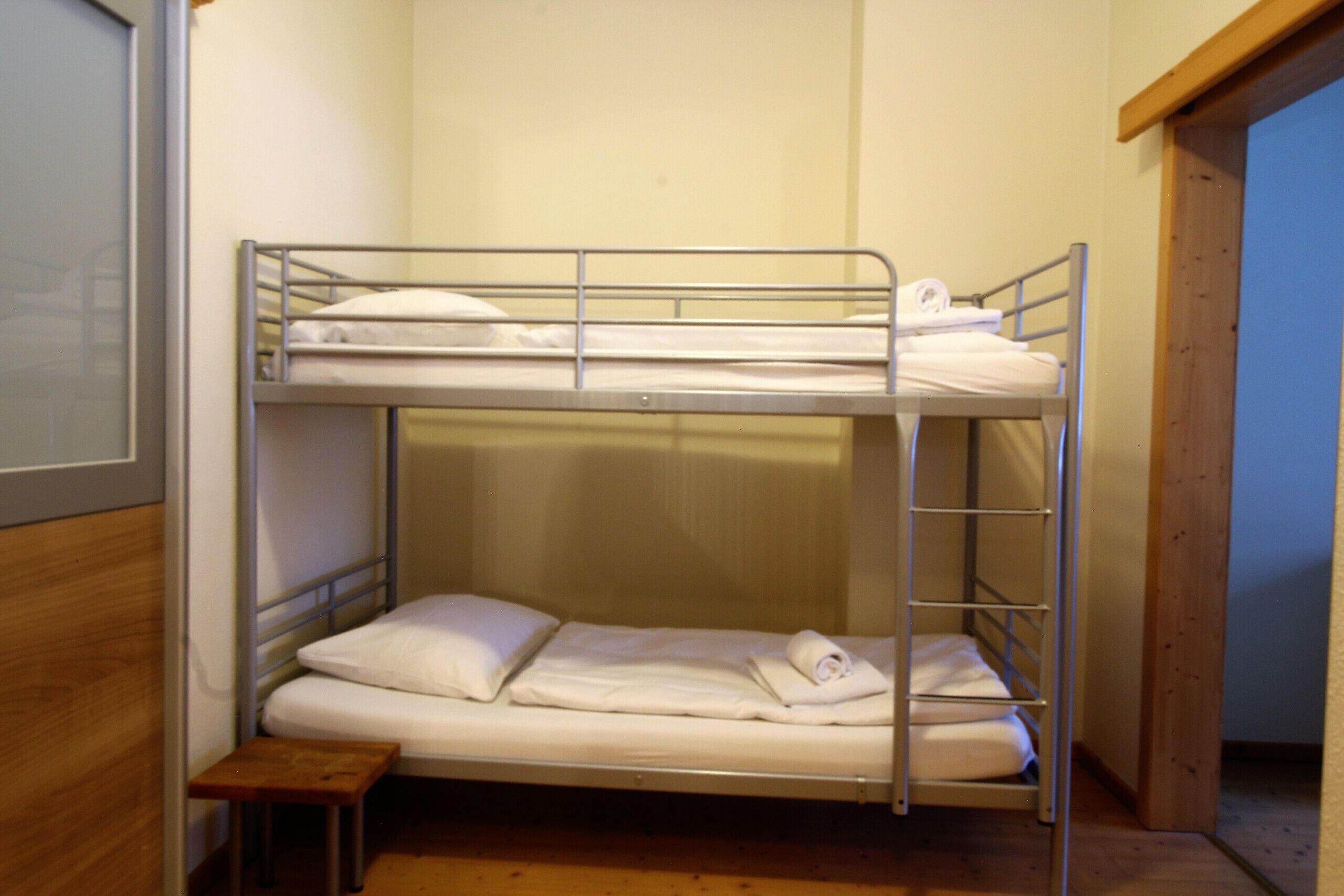 Une chambre avec un lit superposé, un petit tabouret en bois et une échelle en métal.