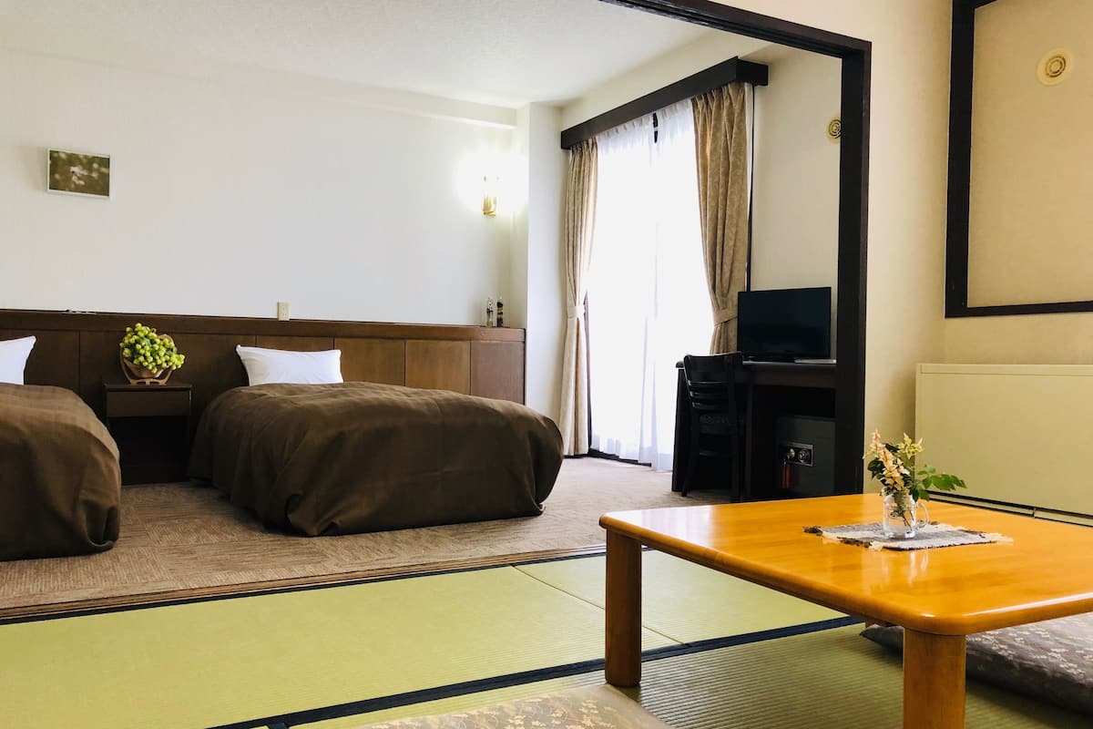 A hotel room with a bed, a small table, a TV, and a view of the outside through the window.