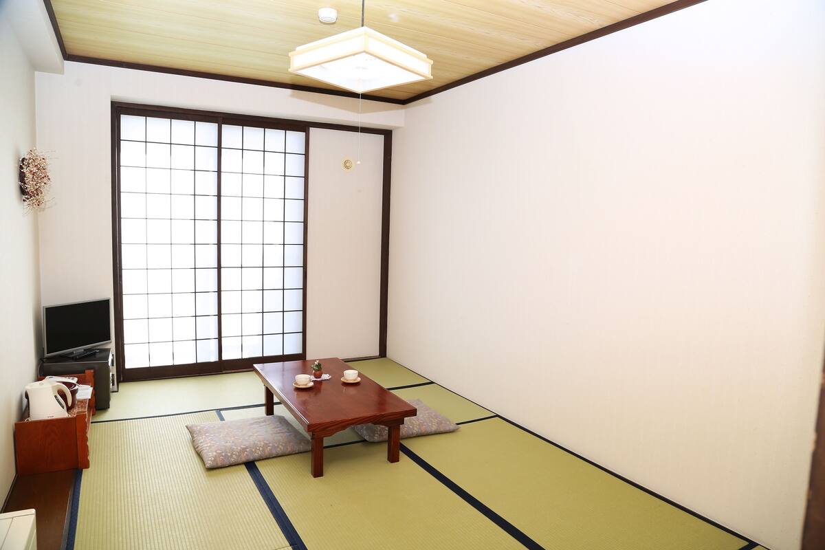 A traditional Japanese room with tatami flooring, a low table with cushions, a sliding door, and a television.