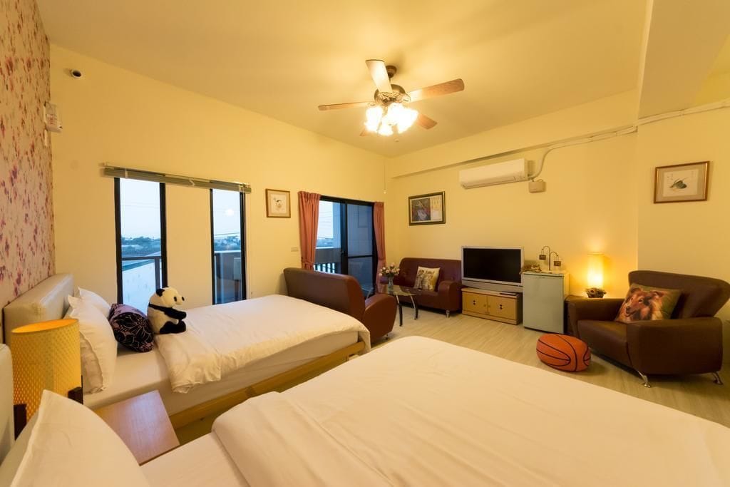 Habitación de hotel con dos camas, televisor, escritorio, silla y balcón con vistas.