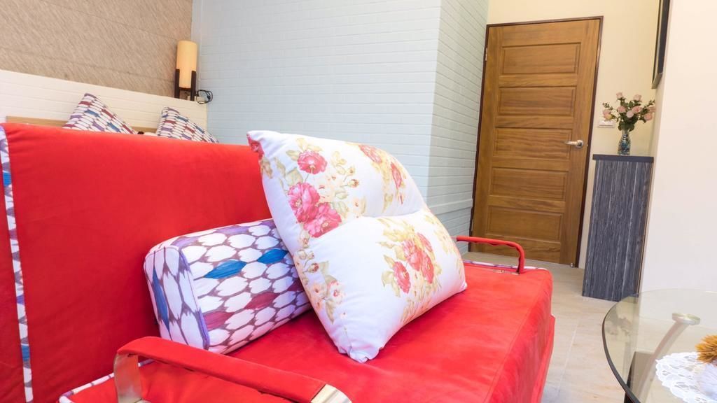 A red sofa with patterned cushions, a wooden door, and a small table with a vase of flowers.