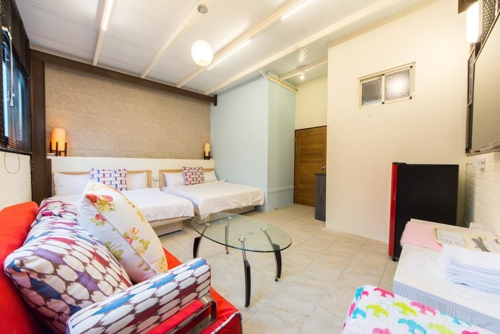A hotel room with two beds, a glass coffee table, a red sofa, and a small TV.