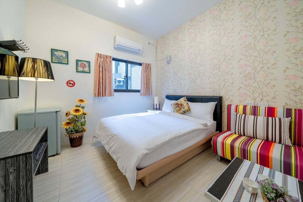 A bedroom with a bed, a sofa, a desk, and a potted plant.
