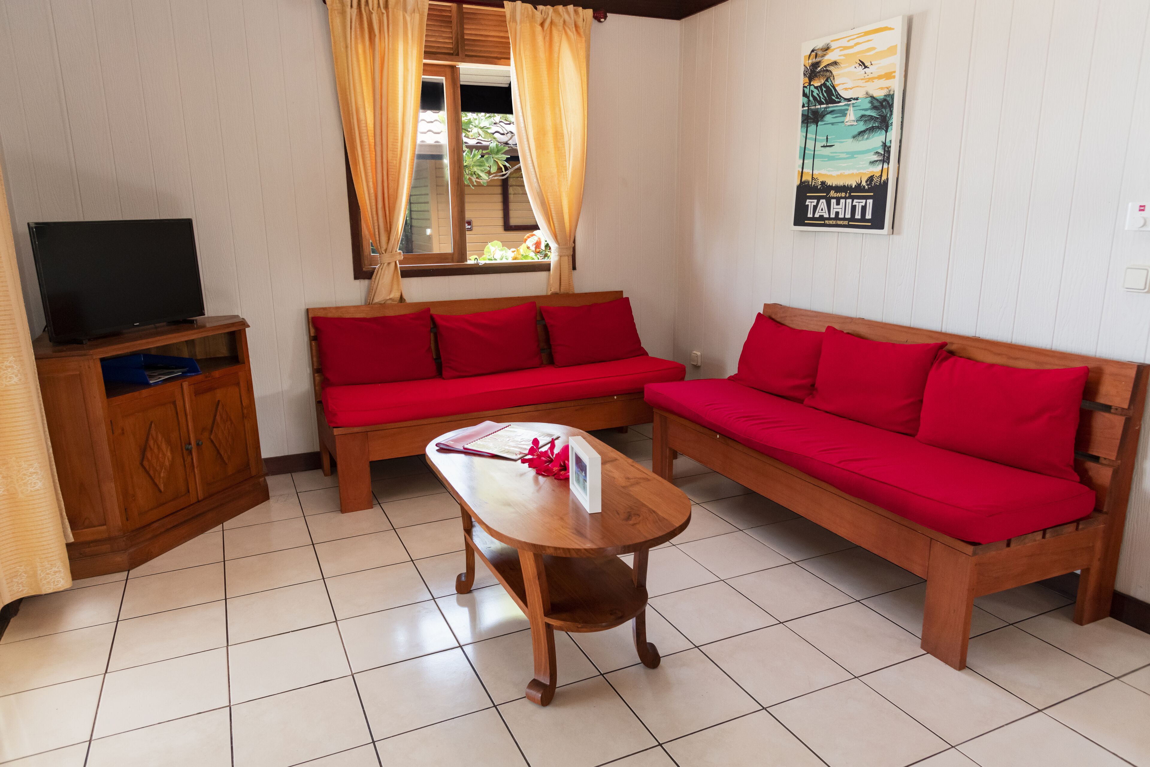 A room with two red sofas, a wooden coffee table, a TV on a stand, and a window with curtains.