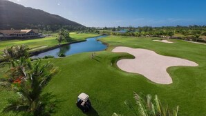 Un parcours de golf avec des obstacles d’eau, des bunkers de sable et un club-house en arrière-plan.