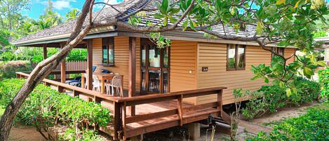 Een houten huis met een terras, omgeven door weelderig groen en bomen.