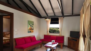 Un salon avec deux canapés rouges, une table basse en bois, un téléviseur posé sur un meuble en bois et une fenêtre avec des rideaux.