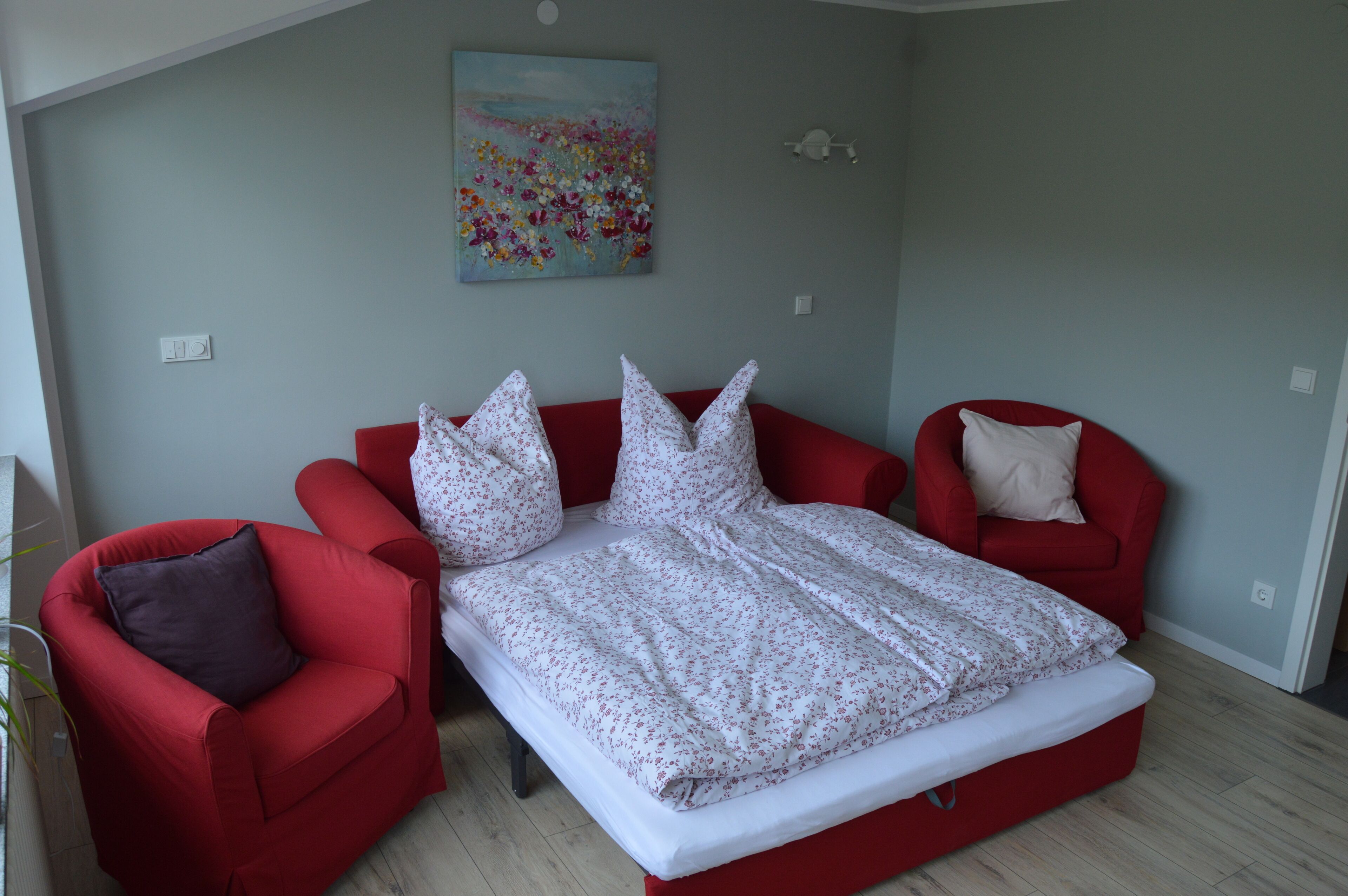 Een slaapkamer met een bed, twee rode stoelen en een schilderij aan de muur.