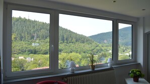 Une pièce dotée de trois grandes fenêtres donnant sur une colline boisée.