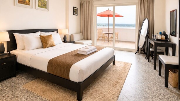 A hotel room with a bed, a desk, a chair, a balcony with an umbrella, and a view of the sea. - Palm34 (Jaipur)