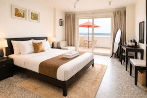Habitación de hotel con cama, escritorio, silla, balcón con sombrilla y vista al mar.