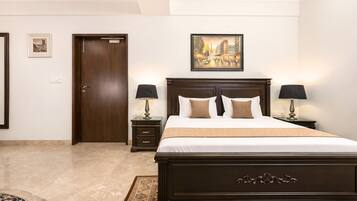 A hotel room with a large bed, two bedside tables with lamps, a door, a framed picture on the wall, and a patterned rug.