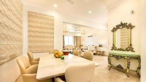 A dining area with a marble table, beige chairs, a decorative mirror, and a sofa in the background. - Palm34 (Jaipur)