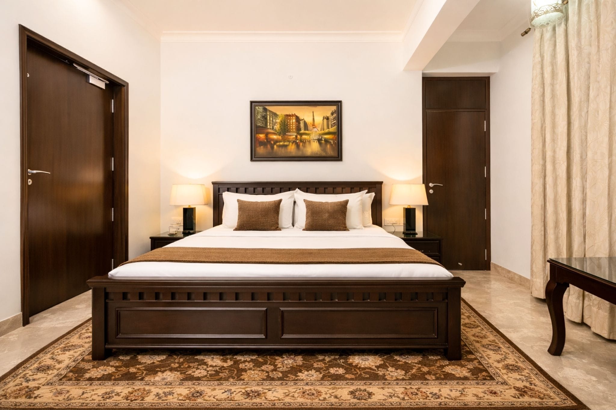 Un dormitorio con una cama grande, dos mesitas de noche con lámparas, un cuadro en la pared y una puerta.