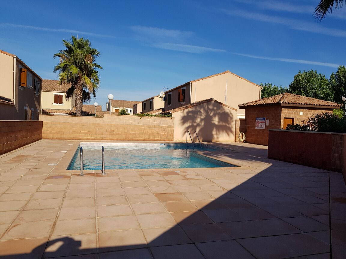 Ein Pool mit Fliesenveranda, umgeben von Gebäuden im mediterranen Stil, darunter Terrakotta-Dächer und Stuckfassaden.