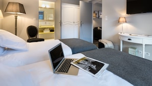 Una habitación de hotel con cama, escritorio, silla, lámpara, ordenador portátil y una revista sobre la cama.