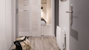 Un pasillo con suelo de madera, un radiador blanco y una puerta que da a un baño con toalla y perchero.
