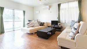 A modern living room with a sofa, coffee table, TV, and a ceiling fan. - Sea Side Yaka (Kin)