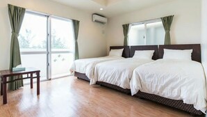 A hotel room with two beds, a wooden table, and a balcony with curtains. - Sea Side Yaka (Kin)