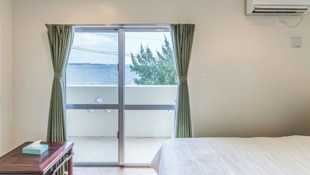 A hotel room with a bed, a wooden table, a window with curtains, and an air conditioning unit. - Sea Side Yaka (Kin)