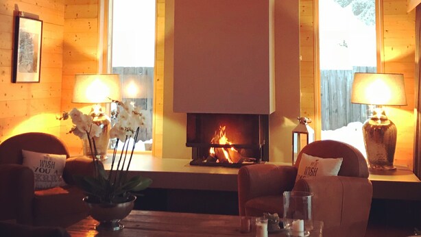 A cozy living room with a fireplace, wooden beams, two windows, and a sofa. - Villars sur Ollon Luxury chalet 600m2 (Villars-sur-Ollon)