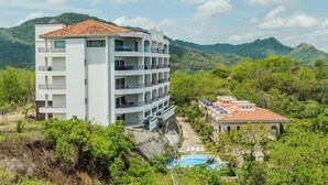 Ein mehrstöckiges Hotel mit Balkonen, umgeben von üppigem Grün und Bergen.