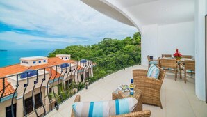Ein Balkon mit Korbmöbeln, Blick auf das Meer und Gebäude im Hintergrund.