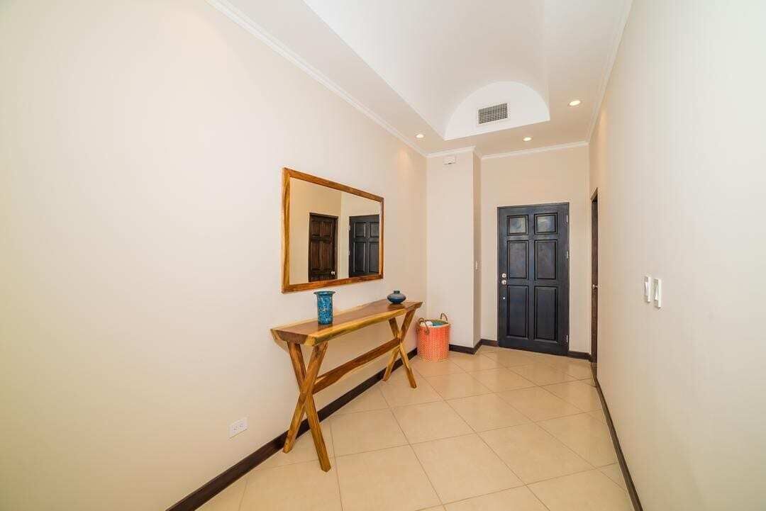 A hallway with a wooden console table, a mirror, a door, and a tiled floor.