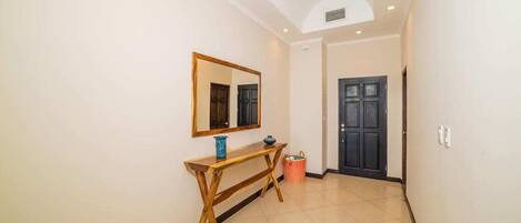 A hallway with a wooden console table, a mirror, a door, and a tiled floor.