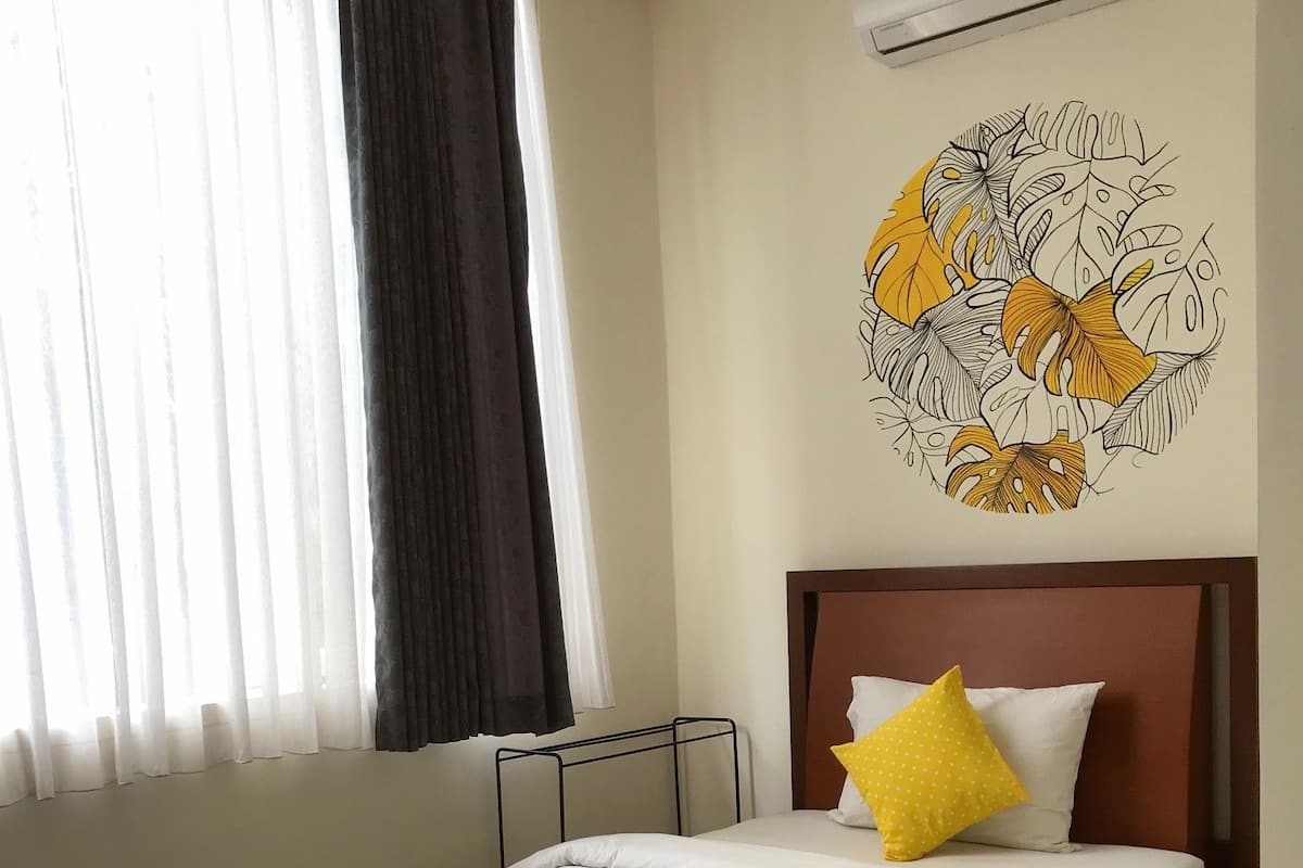 A hotel room with a bed, a wall-mounted air conditioner, and a window with curtains.