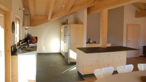 A kitchen with wooden beams, a refrigerator, a sink, and a dining area with chairs. - eco-Chalet in Les Crosets (Valais)