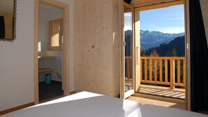 A room with a bed, a bathroom, and a balcony with a mountain view. - eco-Chalet in Les Crosets (Valais)