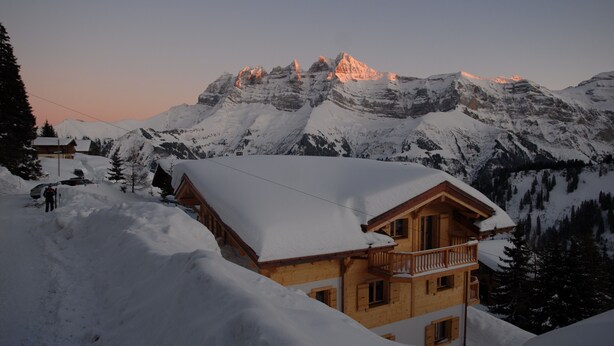 A wooden chalet with a balcony, surrounded by snow-covered mountains and a clear sky. - eco-Chalet in Les Crosets (Valais)