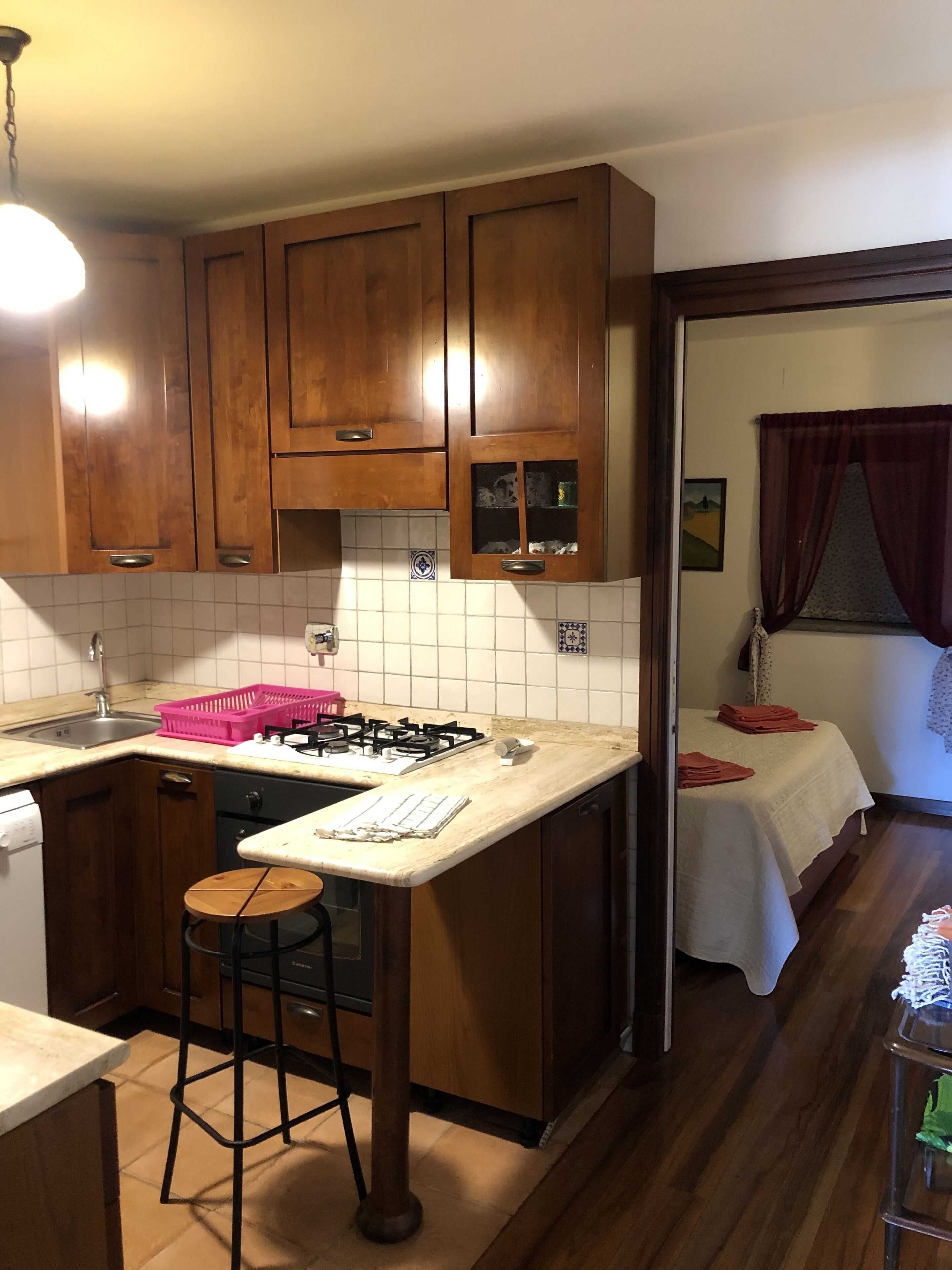 A compact kitchen with wooden cabinets, a gas stove, a sink, and a small bar stool.