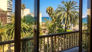 A balcony with a view of a beach, palm trees, and a building in the background.