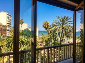 A balcony with a view of a beach, palm trees, and a building in the background.