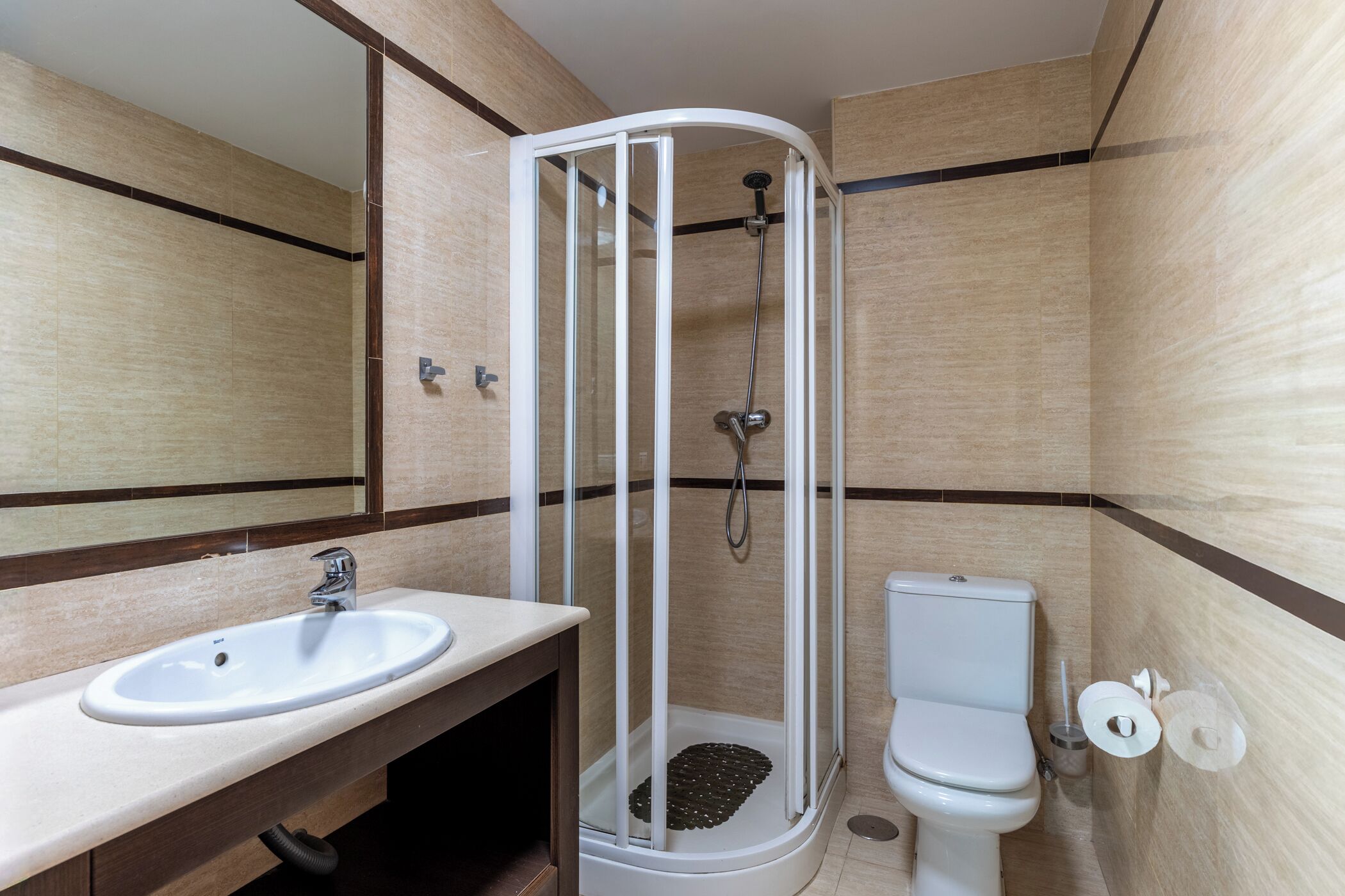 A bathroom with a shower enclosure, a sink, a toilet, and a mirror.