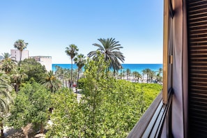 Un balcon avec vue sur l’océan, les palmiers et les bâtiments.