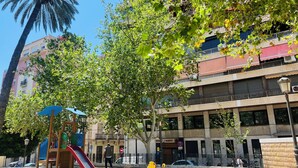 A playground with a slide and swings, a palm tree, and a building with balconies and a sign for 'Hotel PASETTO'.