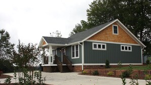 A two-story house with a covered porch, a brick foundation, and a sloped roof. - Ridge Cottage Residence (Campobello)