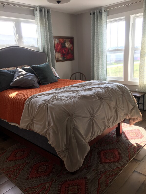 A bedroom with a bed, a headboard, a painting, a window, and a view of the outdoors.