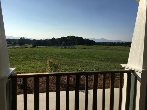 En balkon med udsigt over en græsplæne, en hvid bygning og fjerne bjerge.