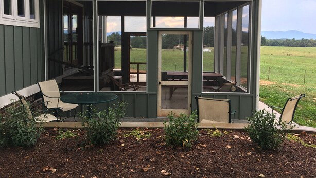 A covered patio with a table and chairs, a bench, and a view of a grassy field and mountains. - Ridge Cottage Residence (Campobello)