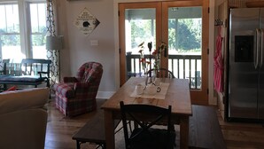 A cozy dining area with a wooden table, chairs, and a chandelier. There is a sign on the wall and a refrigerator in the background. - Ridge Cottage Residence (Campobello)