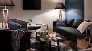 Un soggiorno moderno con un divano blu scuro, una poltrona abbinata, un tavolino da caffè con libri e bicchieri, e una televisione a schermo piatto appesa al muro.