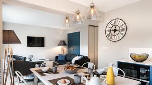 Una cucina moderna con zona pranzo, caratterizzata da un tavolo bianco apparecchiato per la colazione, una grande sveglia a parete e un armadietto blu.