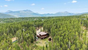 A cabin surrounded by dense forest, with a clear view of distant mountains.
