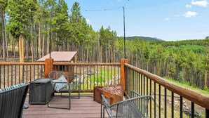 A wooden deck with outdoor furniture, a fire pit, and a view of a forested area.